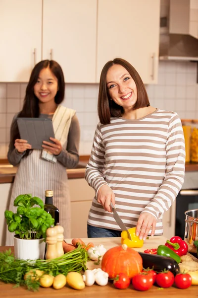 Duas amigas sorridentes estão cozinhando juntas em casa — Fotografia de Stock