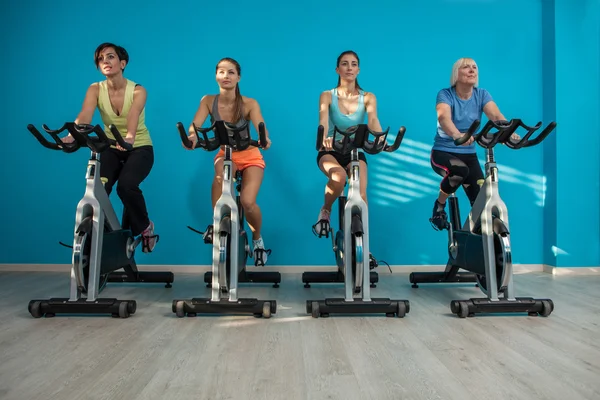 Cuatro mujeres están en bicicleta en el gimnasio — Foto de Stock