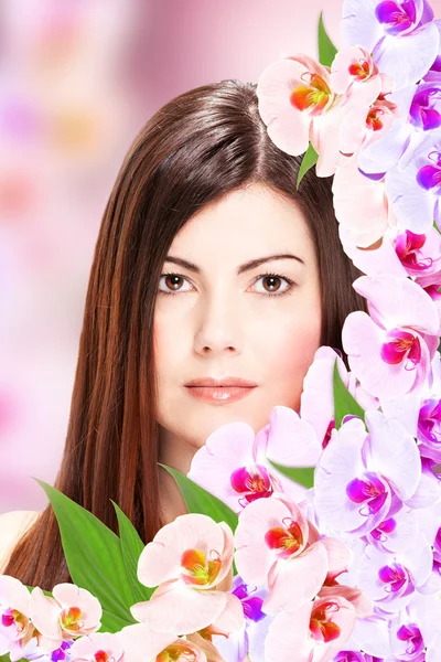 Brunette vrouw met orchideeën naast haar gezicht — Stockfoto