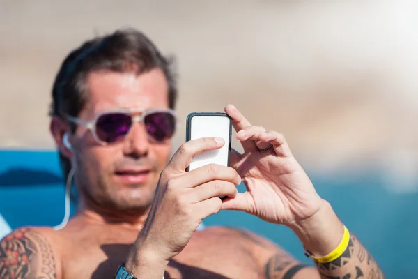 Caucásico hombre está revisando su teléfono mientras se relaja en la playa — Foto de Stock