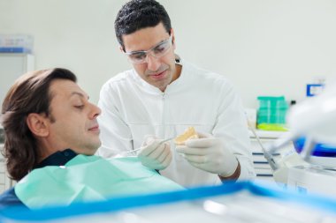 Dentist is showing a plaster model to his patient  clipart