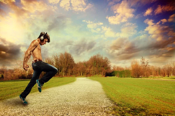 Танцовщица без рубашки с наушниками на фоне пейзажа — стоковое фото