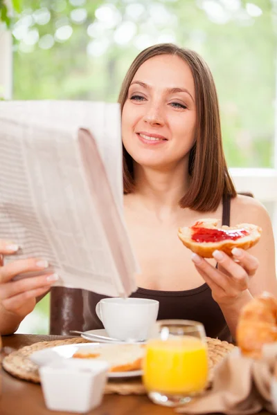 Woman is reading the newspaper while having breakfast — Stock Photo, Image