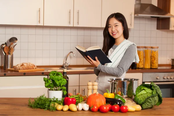 Asiática sonriente mujer buscando un libro de cocina — Foto de Stock