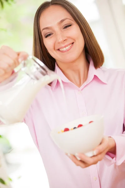 Mujer sonriente está vertiendo una leche en copos de maíz — Foto de Stock