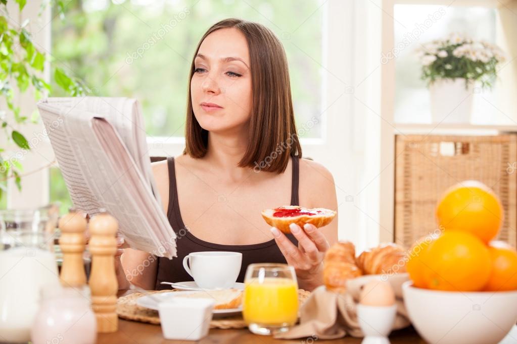 woman is reading the newspaper while having breakfast