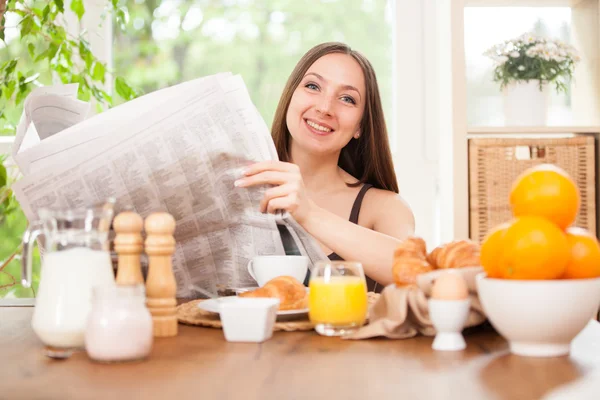 Mulher está lendo um jornal enquanto toma café da manhã — Fotografia de Stock
