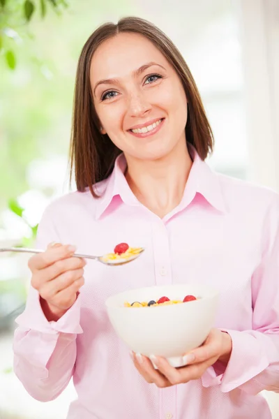 Lachende vrouw verkeert cornflakes met bessen bij het ontbijt — Stockfoto