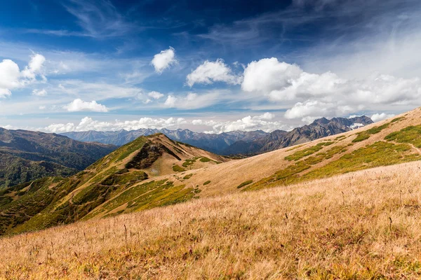 La pintoresca vista superior sobre el valle entre las montañas del Cáucaso. Pendientes de colinas con hierba amarilla seca sobre un fondo de cielo azul con nubes en el otoño —  Fotos de Stock