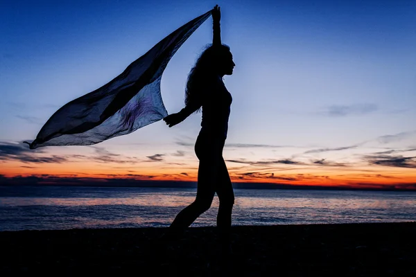 Silhouette of woman dancing against sunset sun at the seashore  with her pareo — Stock Photo, Image