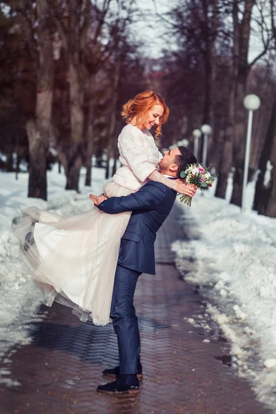 Elégant ascenseur marié élégant sur ses mains mariée dans un parc enneigé — Photo