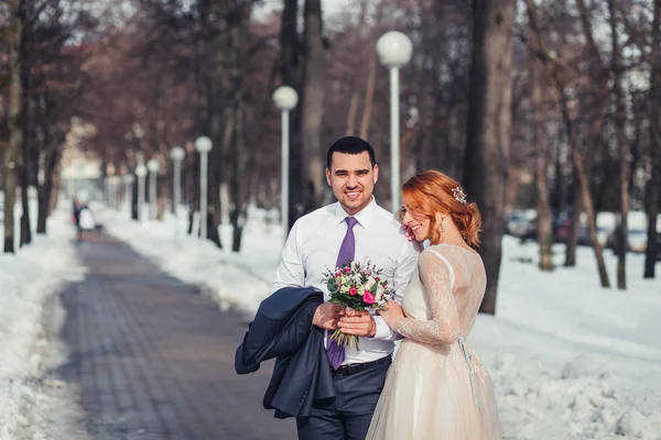 Redhead bride and groom hugging in the snowy spring park — Stock Photo, Image