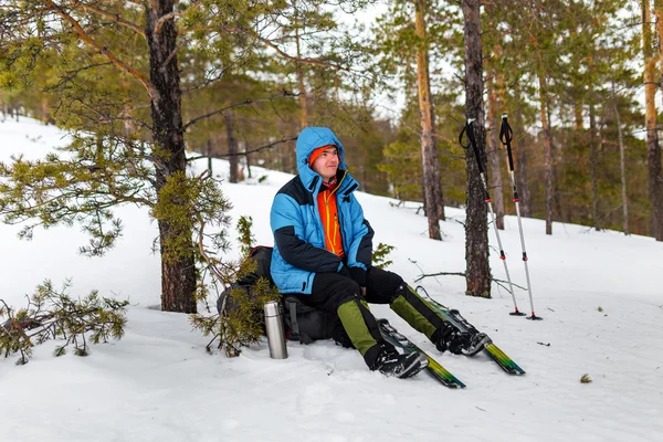 Touristenwanderer im Winterwald sitzt auf einem Rucksack und lächelt — Stockfoto