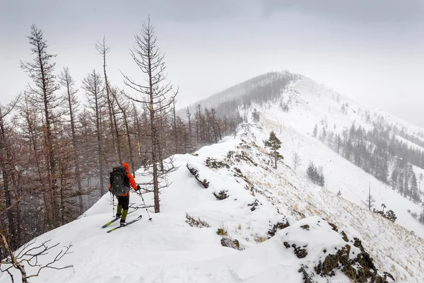 Hombre con esquís y mochila de pie en un sendero en la cima de la montaña — Foto de Stock
