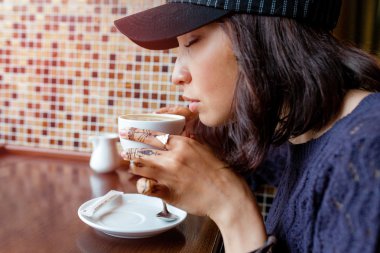 Kız yol kenarı kafede kahve içiyor. Tonda sıcak renkler