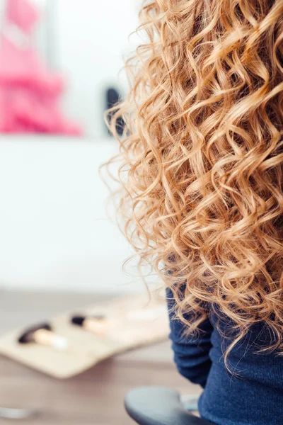 Länge kvinnliga blont lockigt hår under hårbehandling med locktång, närbild, på frisör interiör bakgrund — Stockfoto