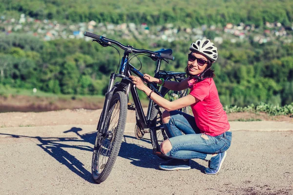 Fröhliche junge Frau sitzt neben dem Fahrrad und überprüft es — Stockfoto