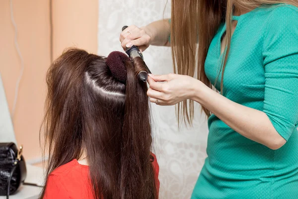 Estilista no salão de barbeiro usando ferro de ondulação para cabelo morena cur — Fotografia de Stock