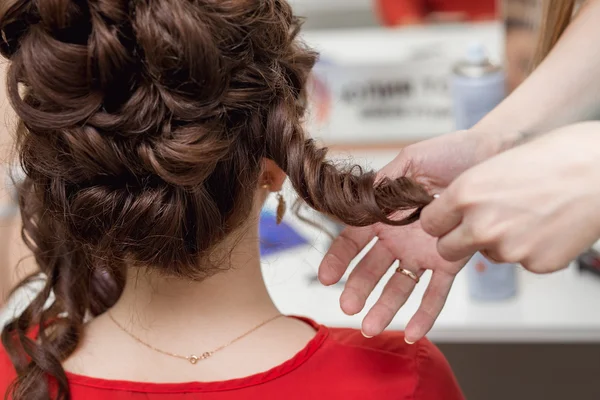 Professional hairdresser styling long woman curly hair. Emotional detail of the hands making hairstyle at hair salon. Color toned image. Blurred background. — Stock Photo, Image