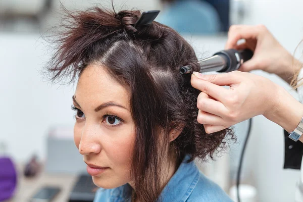 Женщина парикмахер делает прическу с помощью щипцов для волос в течение длительного времени h — стоковое фото