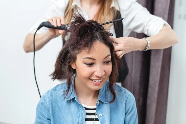 Женщина парикмахер делает прическу с помощью щипцов для волос в течение длительного времени h — стоковое фото