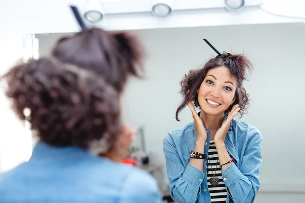 A young woman checks and corrects her hair in the mirror in a ha — Stock Photo, Image