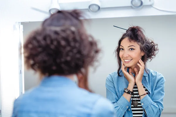 A young woman checks and corrects her hair in the mirror in a ha — Stock Photo, Image