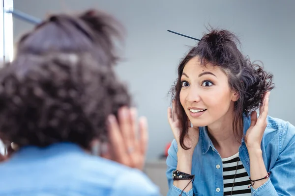 A young woman checks and corrects her hair in the mirror in a ha — Stock Photo, Image