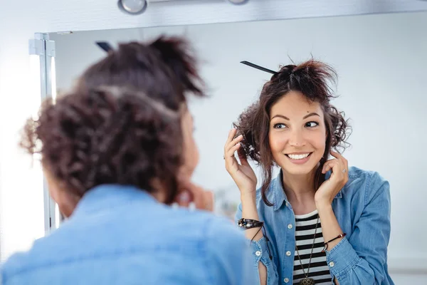 A young woman checks and corrects her hair in the mirror in a ha — Stock Photo, Image