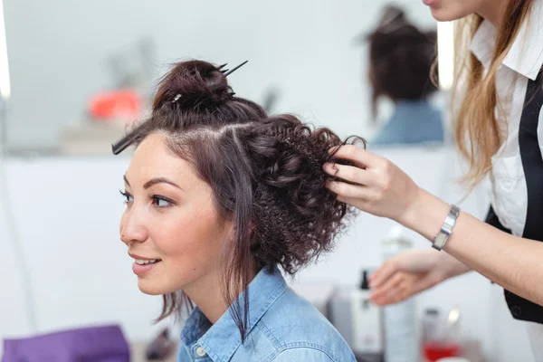 Cabeleireiro fazendo argolinhas para uma mulher morena feliz. Cabelos — Fotografia de Stock