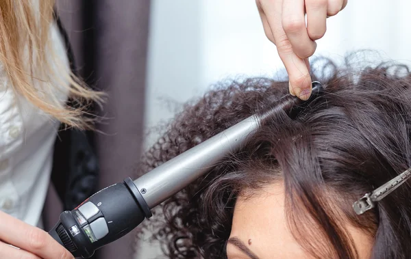 Close-up de uma mulher cabeleireira fazendo cachos no cabelo marrom longo — Fotografia de Stock