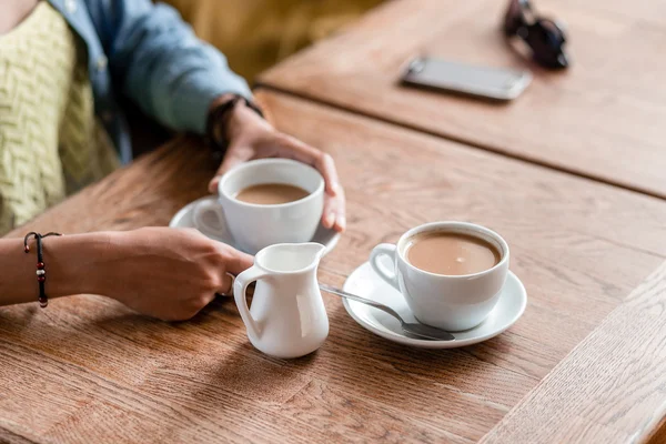 Две чашки кофе с женскими руками на деревянном столе в кафе — стоковое фото