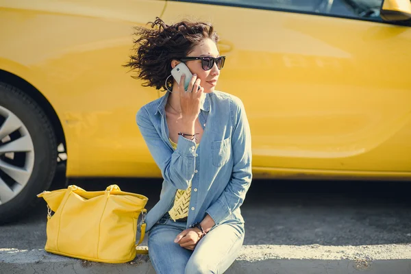 Mujer joven sentada junto a coche amarillo y hablando en un móvil p —  Fotos de Stock