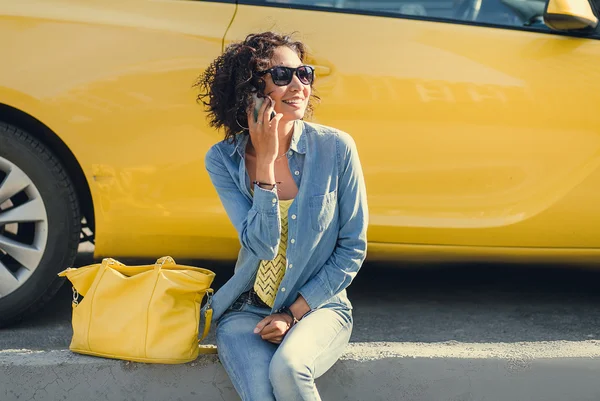 Mujer joven sentada junto a coche amarillo y hablando en un móvil p —  Fotos de Stock