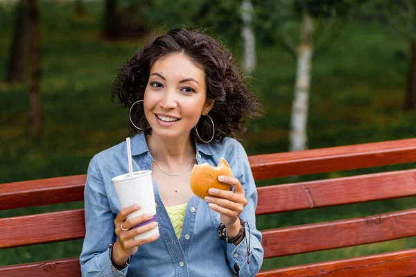 Young woman enjoying a fast food chicken burger and soda water o