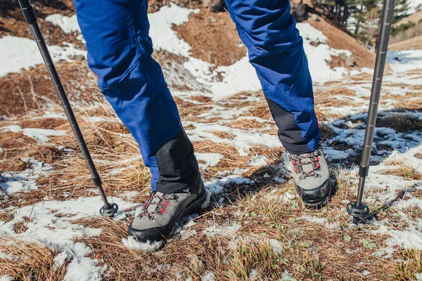 Primer plano de botas de senderismo y palos en la hierba cubierta de nieve a principios de primavera en las montañas — Foto de Stock
