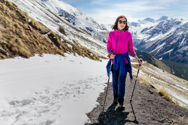 Caminante mujer caminando por sendero de montaña con bastones de senderismo, mirando a la vista en la región de Elbrus, montañas del Cáucaso —  Fotos de Stock