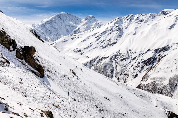 mountaineering group of tourists climbing up the snow covered mountain on the background of Caucasus Range. The steep slope and a snowstorm on a clear day