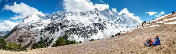 Активная женщина в заснеженных горах Кавказа, милая девушка, сидящая на холме высокой горы, покрытой снегом, концепция весенних каникул — стоковое фото