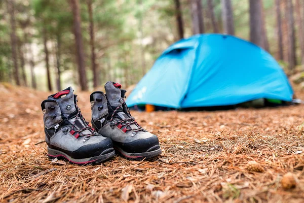 Trekking túra bakancs, háttérben a kék turisztikai sátortábor vad erdőben — Stock Fotó