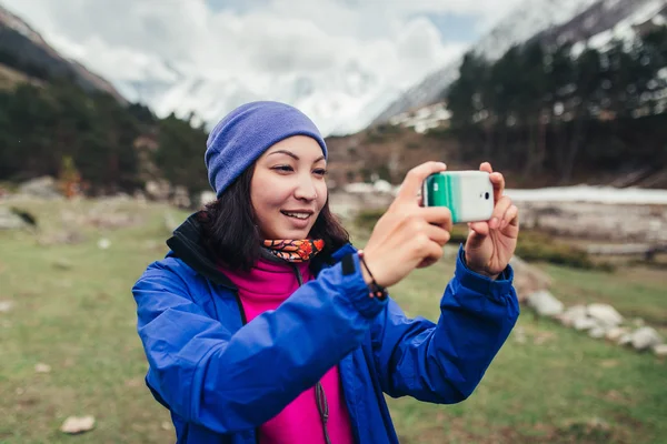 Fiatal nő túrázó fényképezés okostelefonnal a hegyekben csúcs tavasszal — Stock Fotó