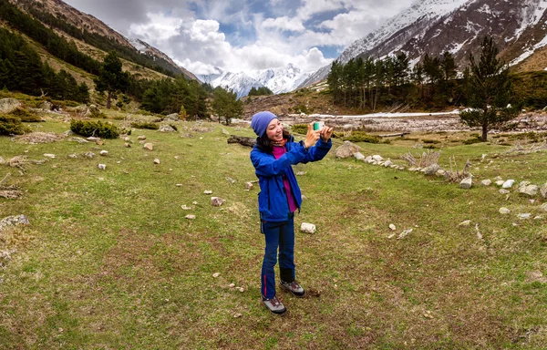 若い女性ハイカーは春に山のピーク時にスマートフォンで写真を撮る — ストック写真