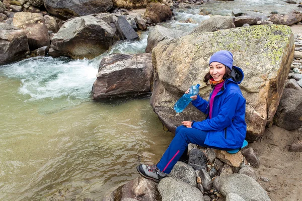 Hiker woman taking water from river in the Swiss mountains on an hiking adventure.