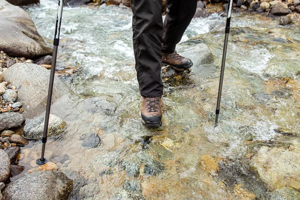 Man in trekking boots hiking outdoor and wading river or creek eith stones on background. Lifestyle, Travel or survival concept top view