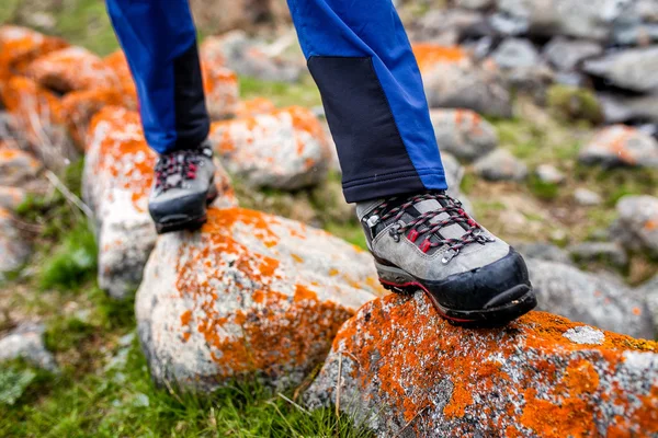 Botas de trekking y senderismo caminando sobre las piedras cubiertas de liquen naranja. Concepto de zapatos de senderismo de calidad — Foto de Stock