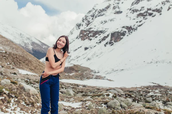 Молодая и счастливая женщина в спортивном бюстгальтере стоит в горах на снегу — стоковое фото
