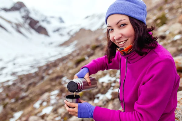 Joven feliz mujer alegre mochilero excursionista vierte té de un termo en las montañas en viaje —  Fotos de Stock