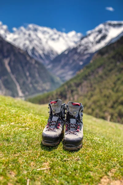 Trekking laarzen op vers gras op zomertijd. Besneeuwde bergen op de achtergrond — Stockfoto