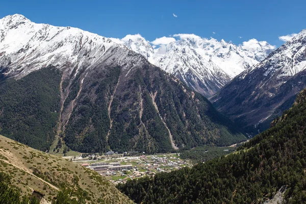 El camino de la montaña y el pueblo en el valle en el fondo de picos nevados —  Fotos de Stock