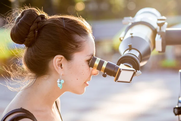 Joven mujer sonriente mirando hacia el cielo a través de telesco astronómico — Foto de Stock